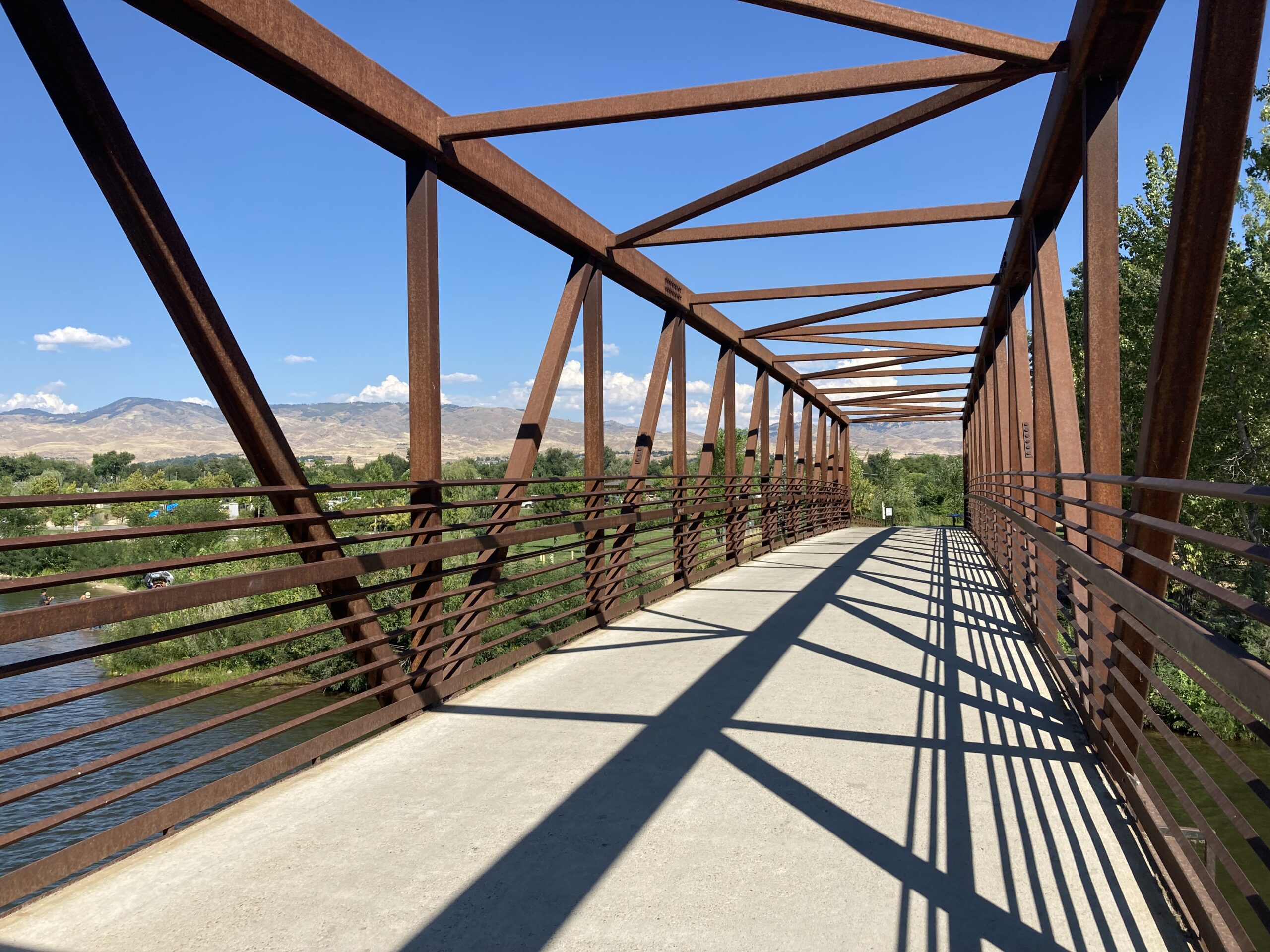 Photo of brown metal bridge path over a river with a blue sky.