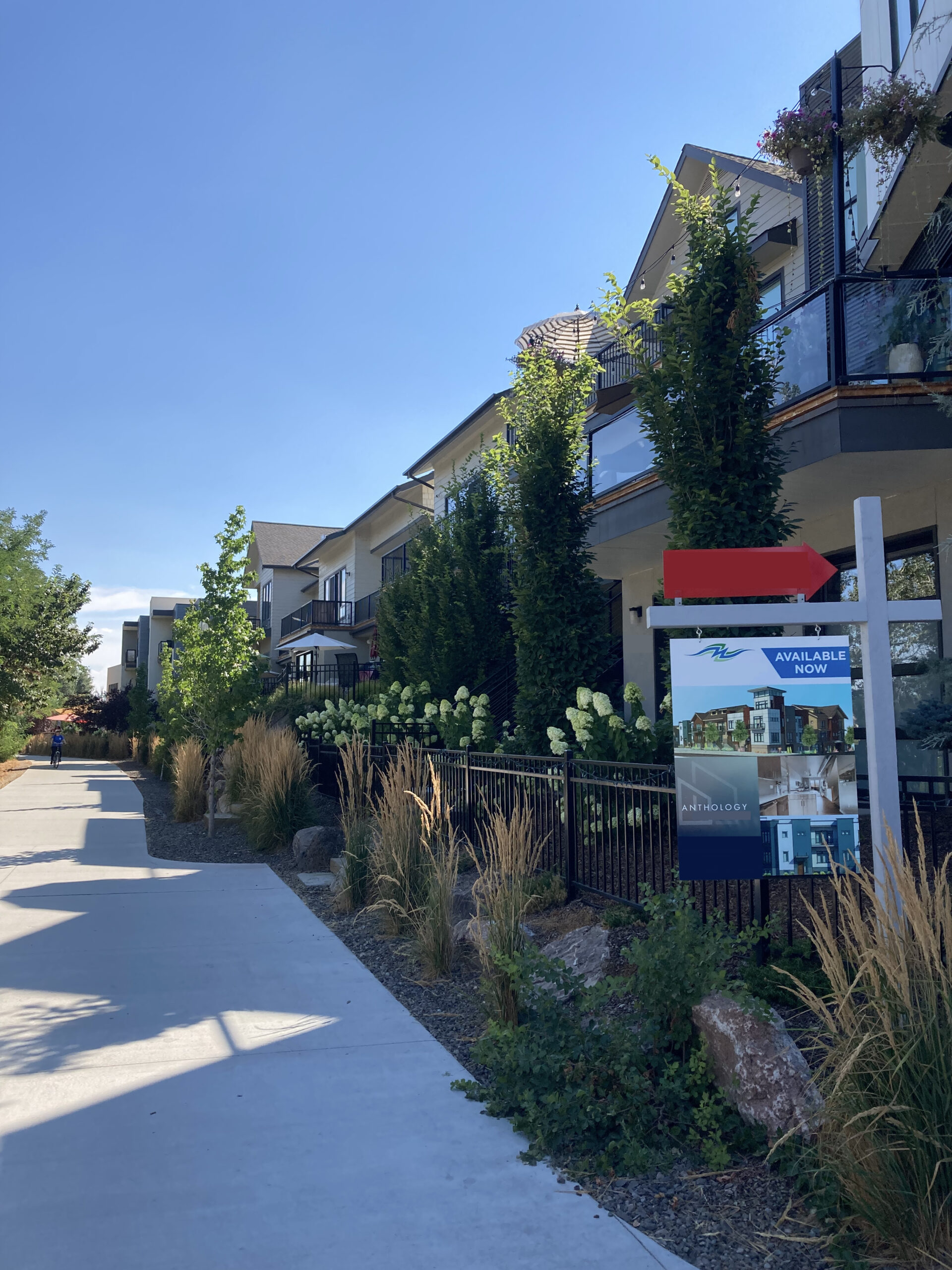 Apartments lining a sidewalk with a for rent/for sale sign.