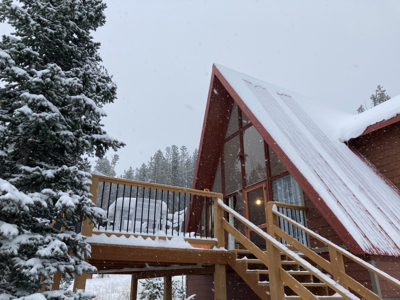 Snowy A-frame cabin with snow covered tree next to it.