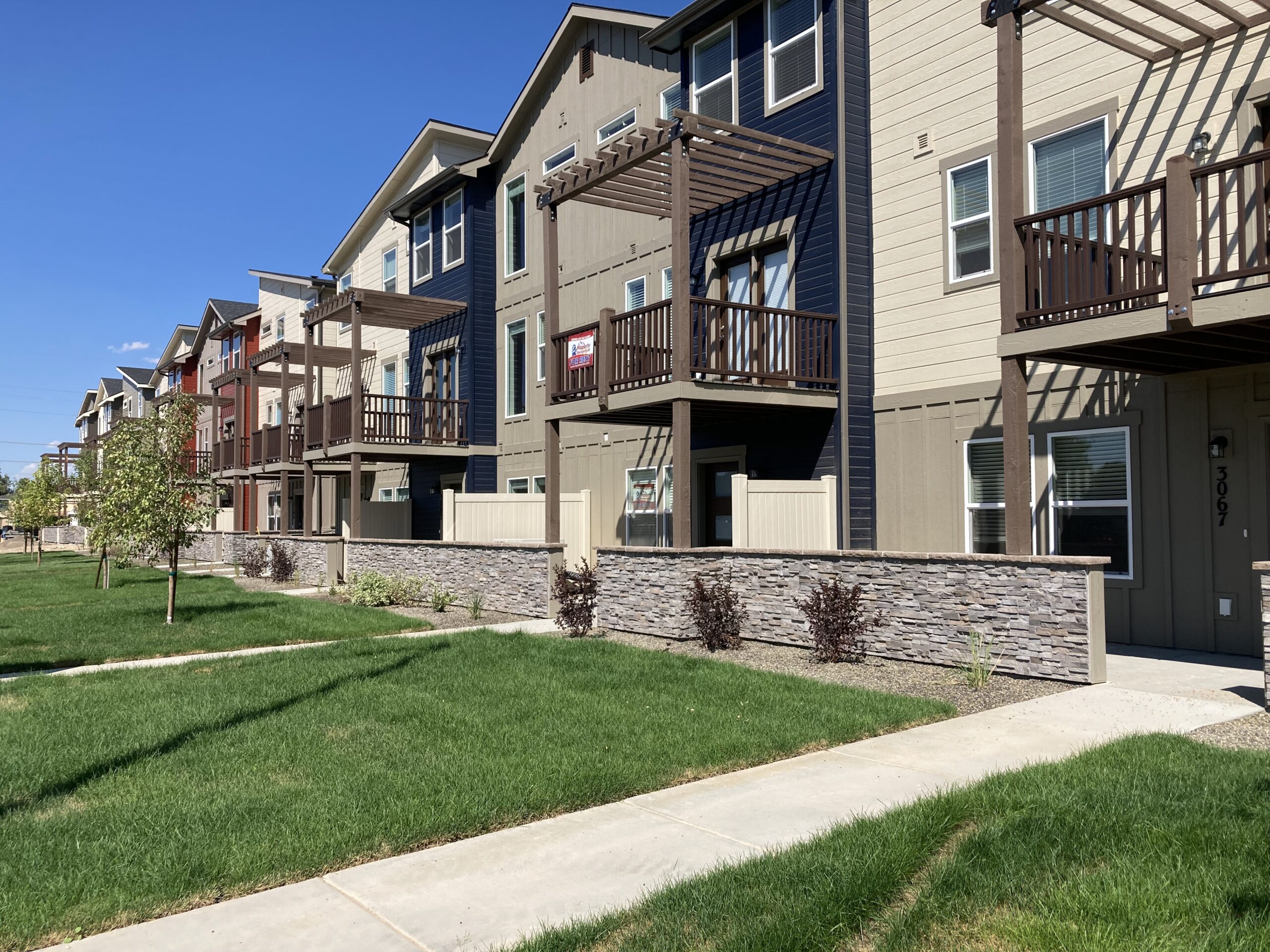 Side by side multi-colored two-story townhouses with green lawns.